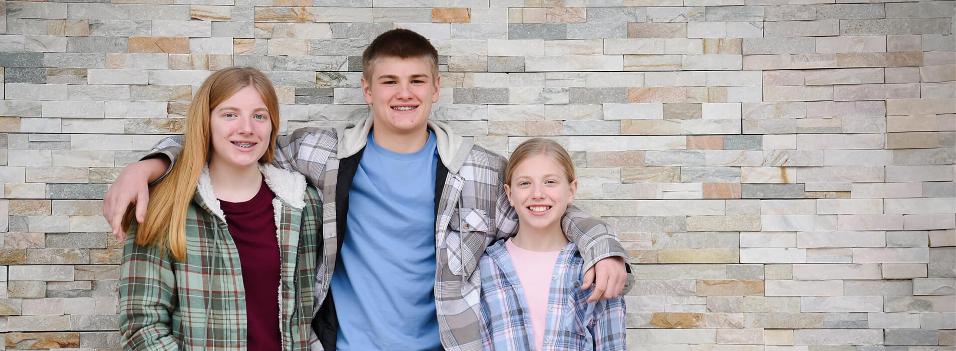 Group of kids standing against a wall smiling.